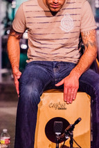 Man sitting on a wooden box playing cajon hands hitting drum percussion