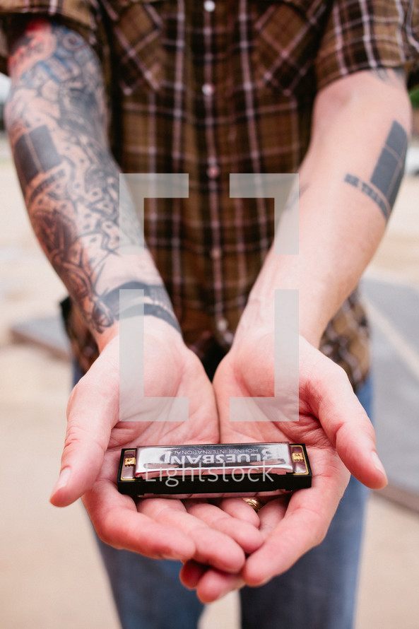 man with tattoos holding a harmonica 