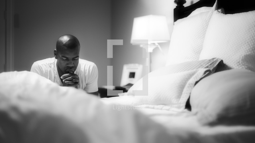 man kneeling in prayer by his bedside 