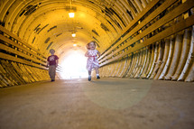 toddler boy and girl running in a tunnel