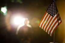 American flag with silhouette of man in lighted background.
