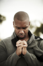 An African American man with head bowed and hands laced in prayer