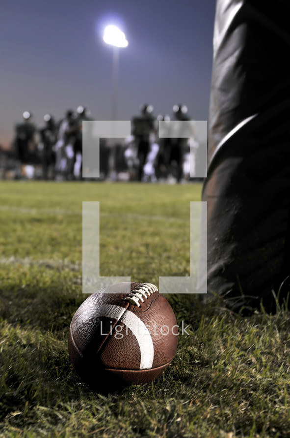 Leg standing by a football on the grass with a silhouette of the team in the background.