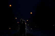 Couple kissing in the snowfall at night.