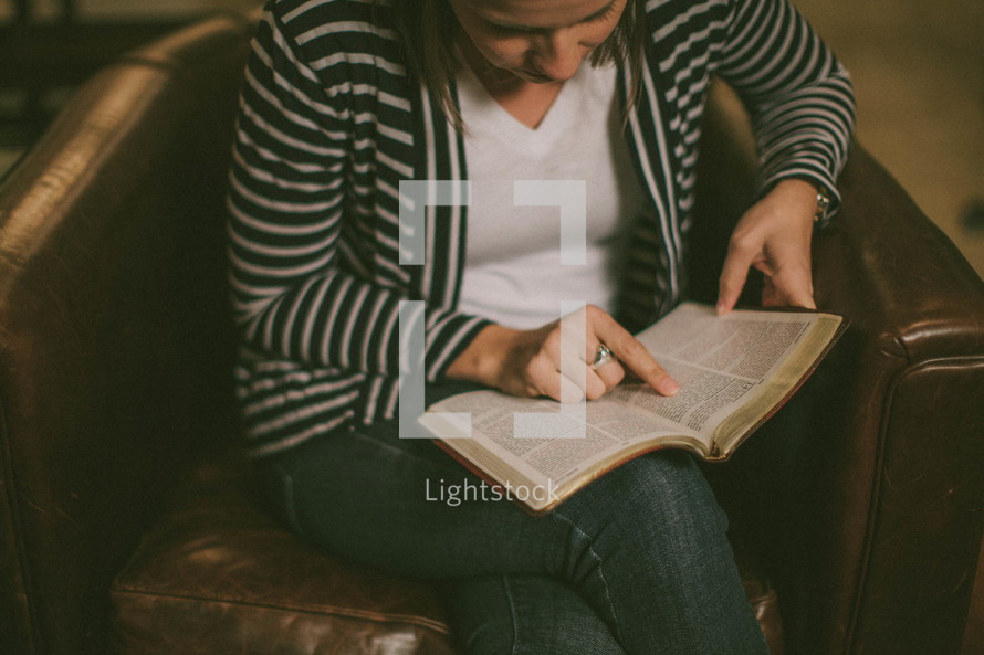 Woman sitting in chair with legs crossed studying the Bible.