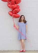 teen girl holding red heart shaped helium balloons 