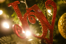 Red glitter "Joy" ornament hanging on Christmas tree.