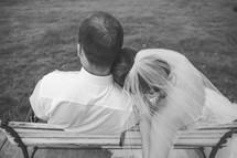 bride and groom sitting on a bench snuggling 