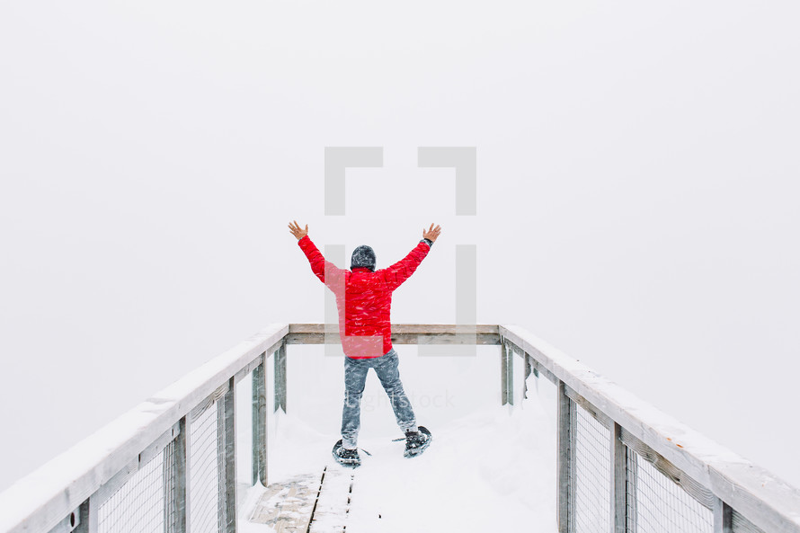 man with raised hands standing on an observation deck in snow 