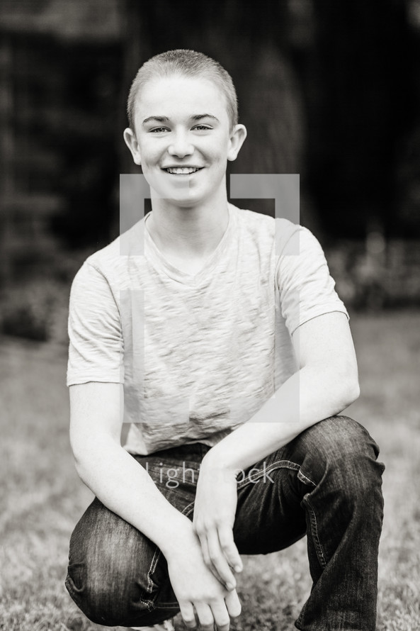 teenage boy squatting and smiling in jeans and T-shirt portrait 