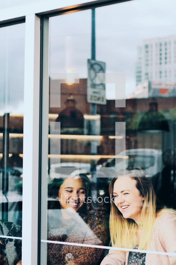 friends laughing sitting in a cafe window 