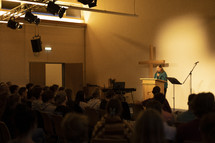 Woman speaking to a group of people with cross behind her