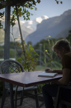Man reading his Bible at a table with snowy mountains in the background