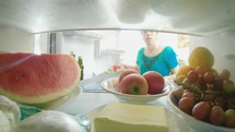 POV shot from inside a refrigerator of a woman opening the door and taking out food