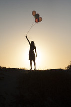 silhouette of a woman holding balloons