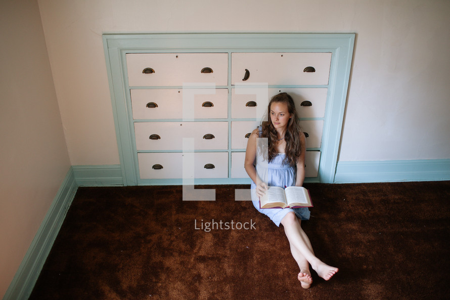 woman reading a bible sitting on the floor in front of a dresser