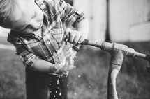 toddler boy washing his hands with an outdoor spigot