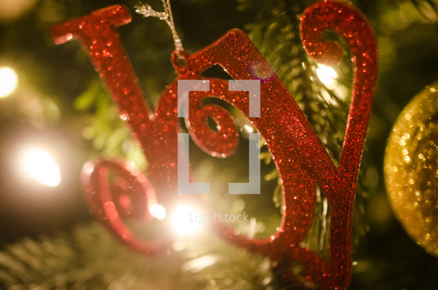 Red glitter "Joy" ornament hanging on Christmas tree.