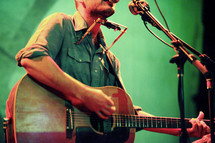 musician on stage playing a guitar and harmonica