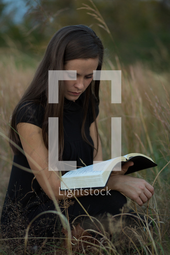close up of woman reading a Bible in a field