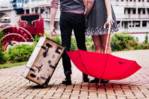 a couple holding a trunk and red umbrella 