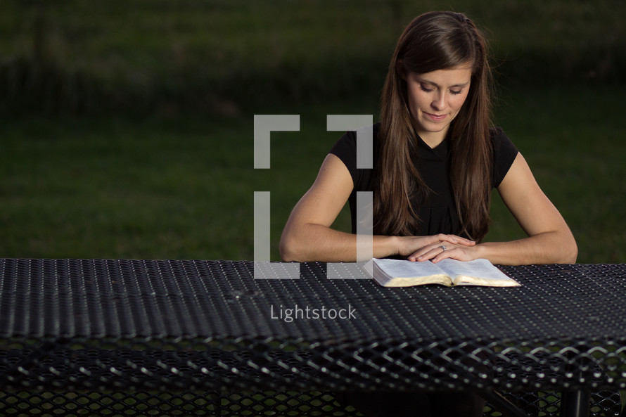 woman sitting at a picnic table reading a Bible