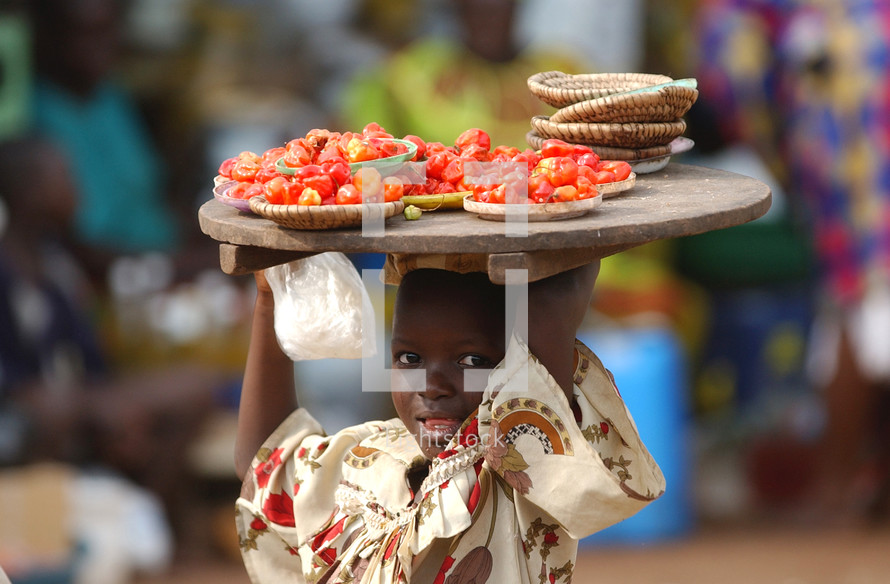 African child carrying a tray of tomatoes on her head in the local market