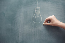 hand drawing a lightbulb on a chalkboard 