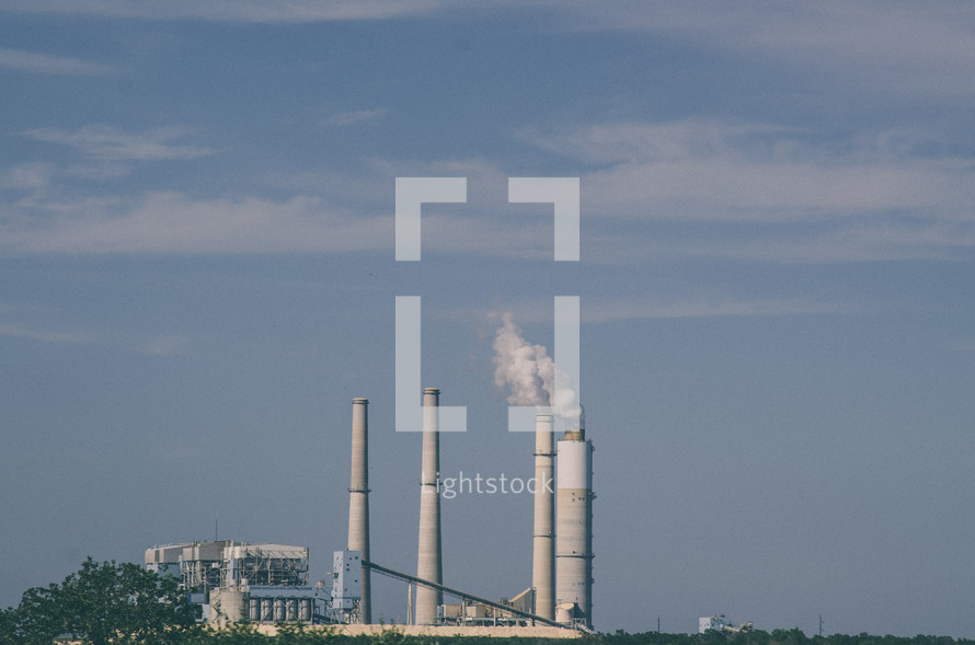 Power plant with smoke rising from a chimney against a blue sky.