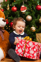 toddler baby girl with gifts near christmas tre