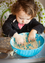 Little baby girl playing with dough on the high chair.