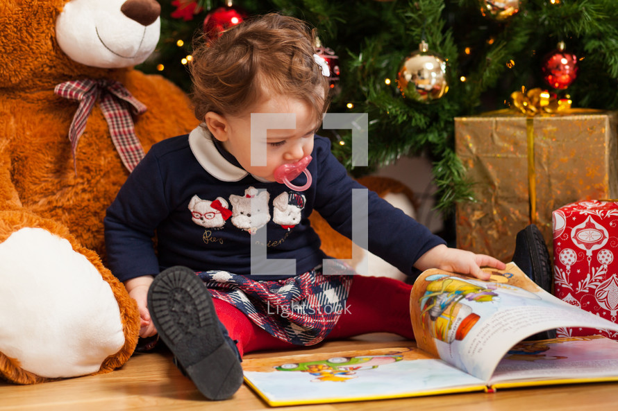 toddler girl with gifts near christmas tree.