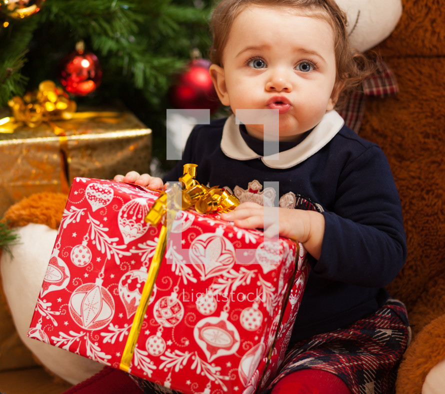 toddler girl with gifts near christmas tree.