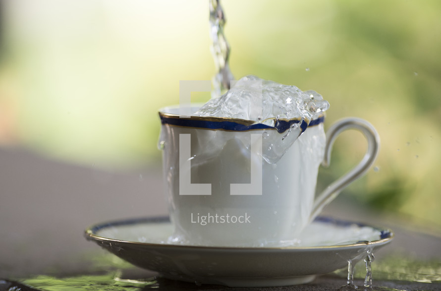 Water being poured and overflowing from a tea cup and saucer.
