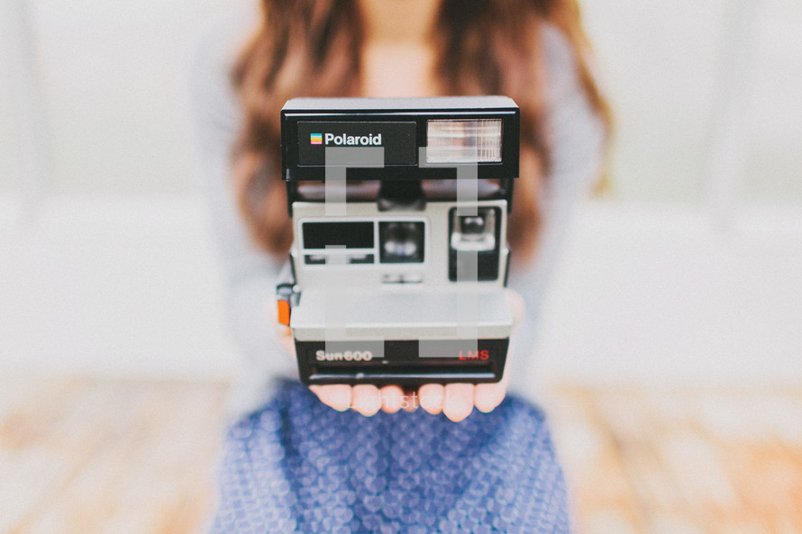 A young woman holds a Polaroid camera