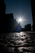Stone cobbles along a side street bank looking towards a cathedral in the distance with the sun beaming through