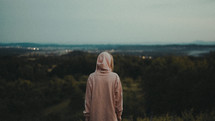 a woman in a hoodie looking out at mountains 