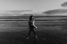 a woman bundled up walking on a beach shore 