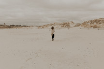 a woman walking on a beach towards sand dunes 