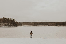 a person standing on a snowy lake shore 