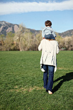 mother walking in the grass with toddler son on her shoulders