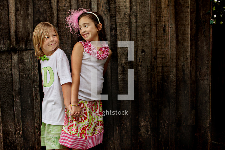 Two young girls holding hands by a wooden fence.