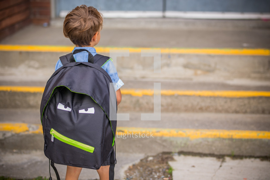 a boy with a backpack standing in front of school doors 