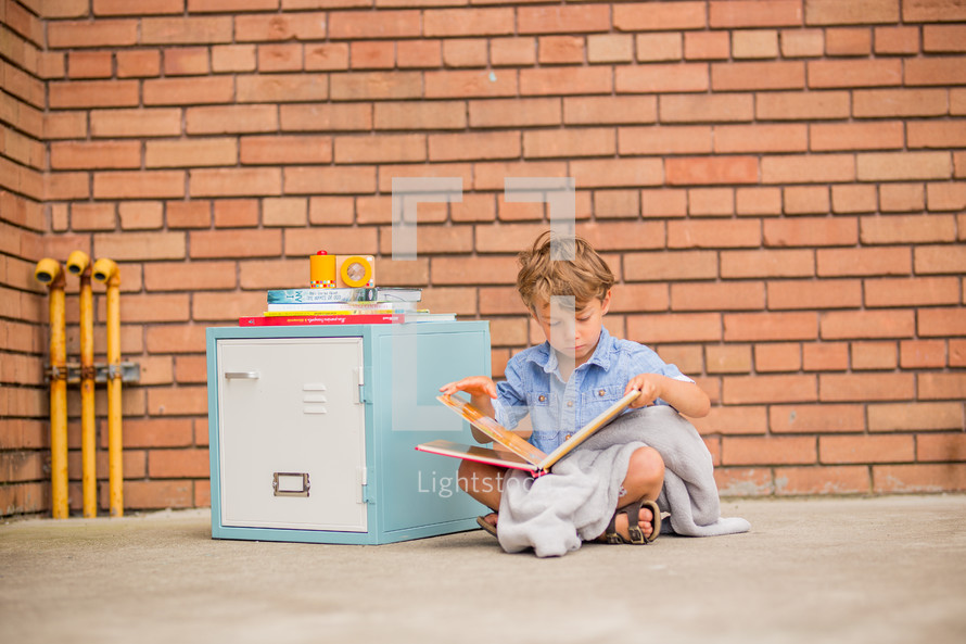 a boy reading a book next to a locker 