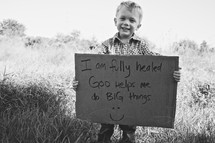 toddler boy holding a sign that reads I am fully healed. God helps me do BIG things.