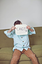 a boy child holding up a sign that reads Candy 