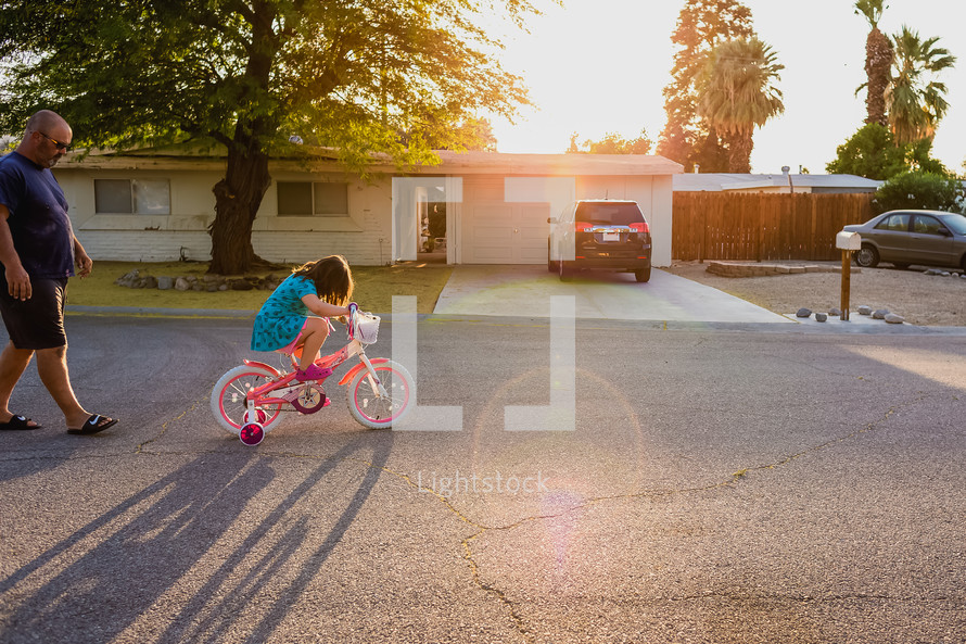 a father watching his daughter ride a bicycle 
