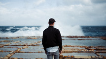 a man standing on a rugged shore watching the waves 