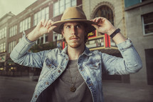 a man in a hat and jean jacket standing in front of a theater marque 
