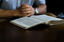 a man sitting on a couch reading a Bible and praying 